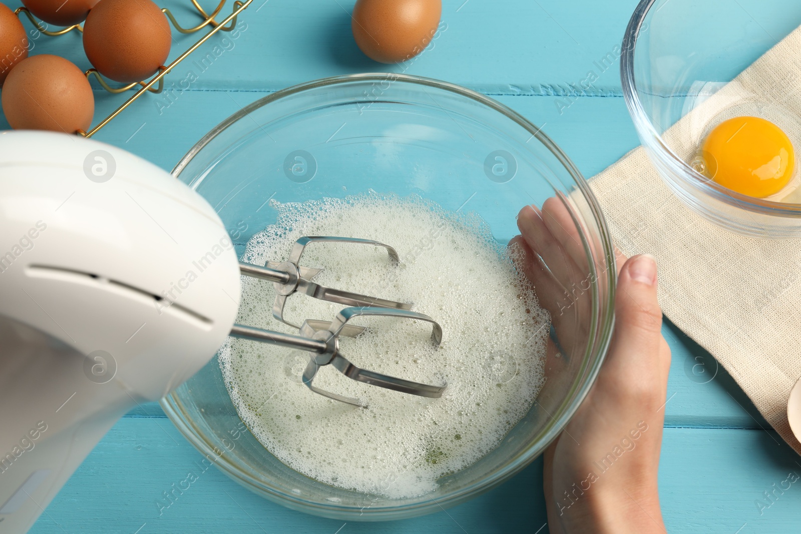 Woman whisking egg whites with hand mixer at light blue wooden table, above view Photo of Woman whisking egg whites with hand mixer at light blue wooden table, above view