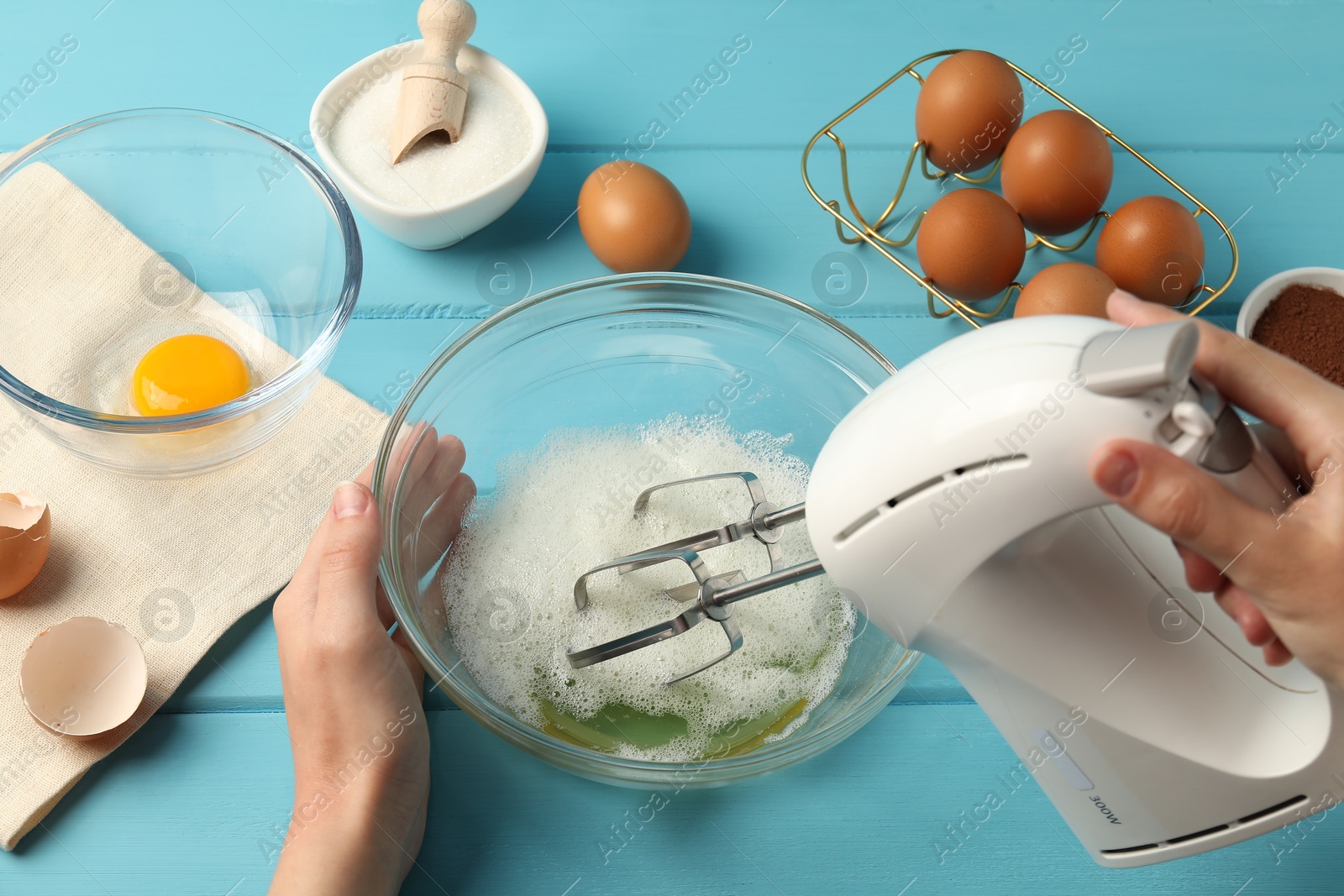 Woman whisking egg whites with hand mixer at light blue wooden table, top view Photo of Woman whisking egg whites with hand mixer at light blue wooden table, top view