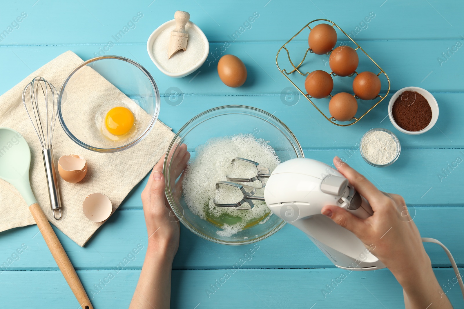 Woman whisking egg whites with hand mixer at light blue wooden table, top view Photo of Woman whisking egg whites with hand mixer at light blue wooden table, top view