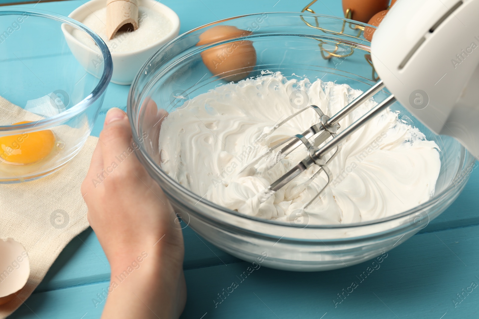 Woman whisking cream with hand mixer at light blue wooden table, closeup Photo of Woman whisking cream with hand mixer at light blue wooden table, closeup