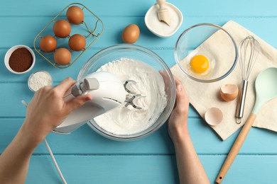 Photo of Woman whisking cream with hand mixer at light blue wooden table, top view