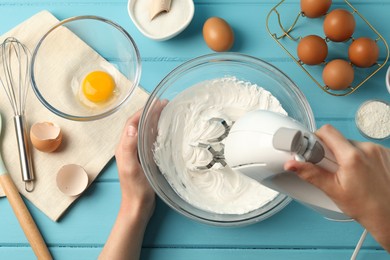 Photo of Woman whisking cream with hand mixer at light blue wooden table, top view