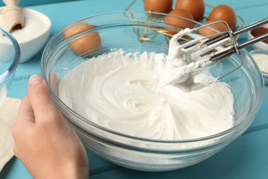 Photo of Woman whisking cream with hand mixer at light blue wooden table, closeup