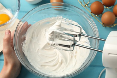 Photo of Woman whisking cream with hand mixer at light blue wooden table, above view