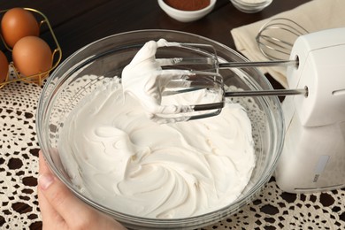 Photo of Woman whisking cream with hand mixer at table, closeup