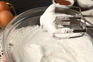 Photo of Hand mixer with whisks and bowl of whipped cream on table, closeup