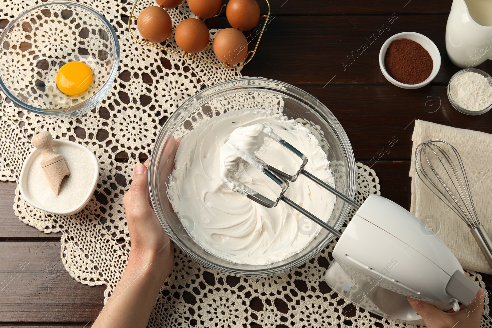 Woman whisking cream with hand mixer at wooden table, top view Photo of Woman whisking cream with hand mixer at wooden table, top view