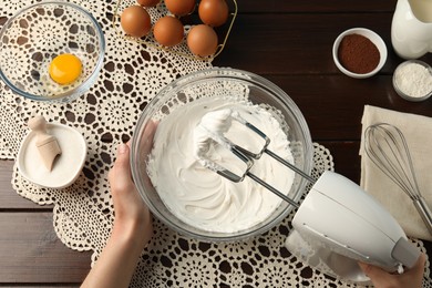 Photo of Woman whisking cream with hand mixer at wooden table, top view