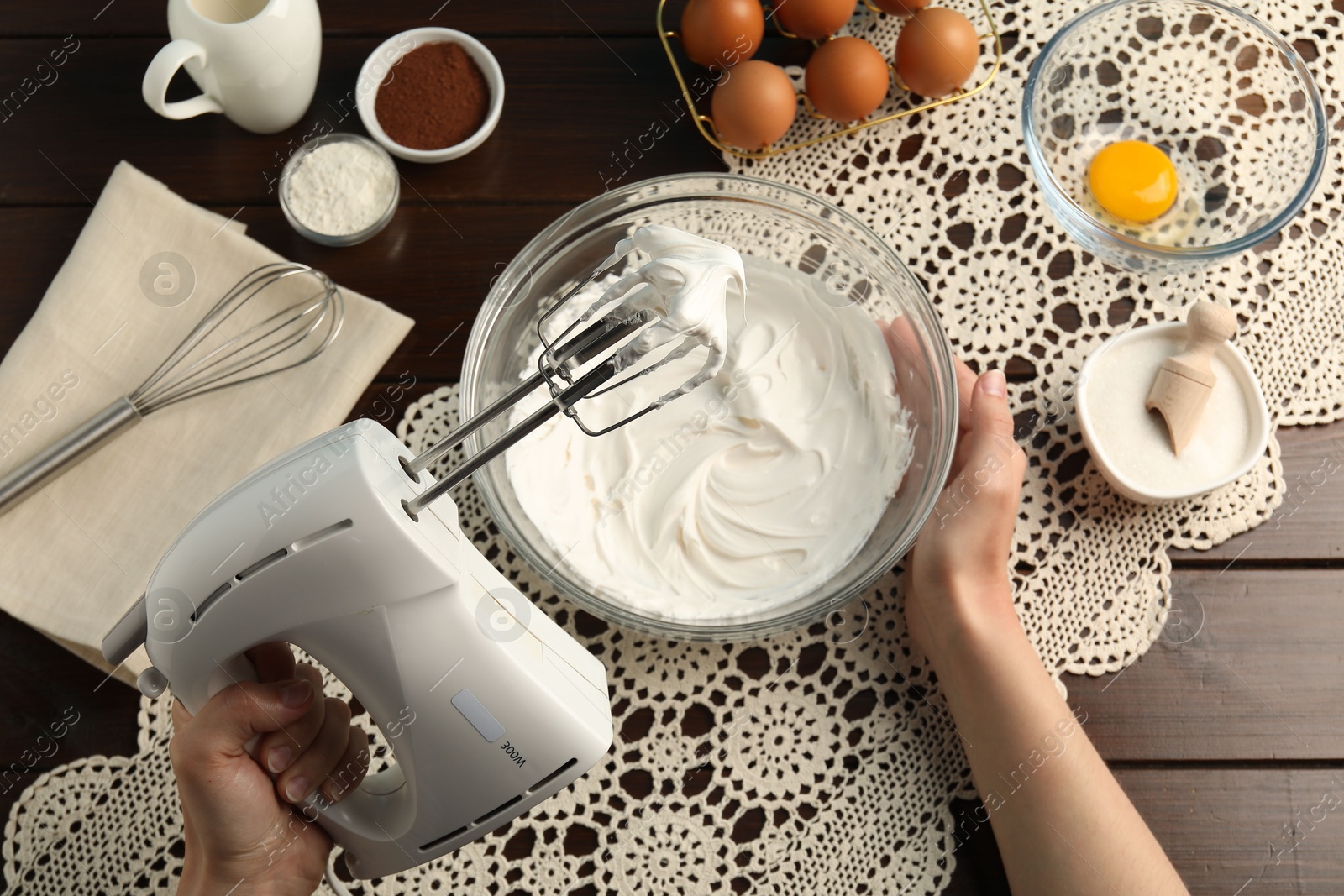 Woman whisking cream with hand mixer at wooden table, top view Photo of Woman whisking cream with hand mixer at wooden table, top view