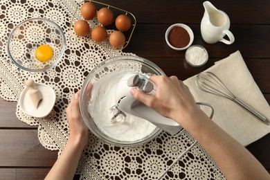 Photo of Woman whisking cream with hand mixer at wooden table, top view