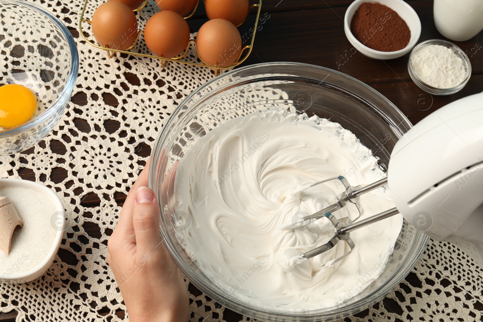 Woman whisking cream with hand mixer at table, above view Photo of Woman whisking cream with hand mixer at table, above view
