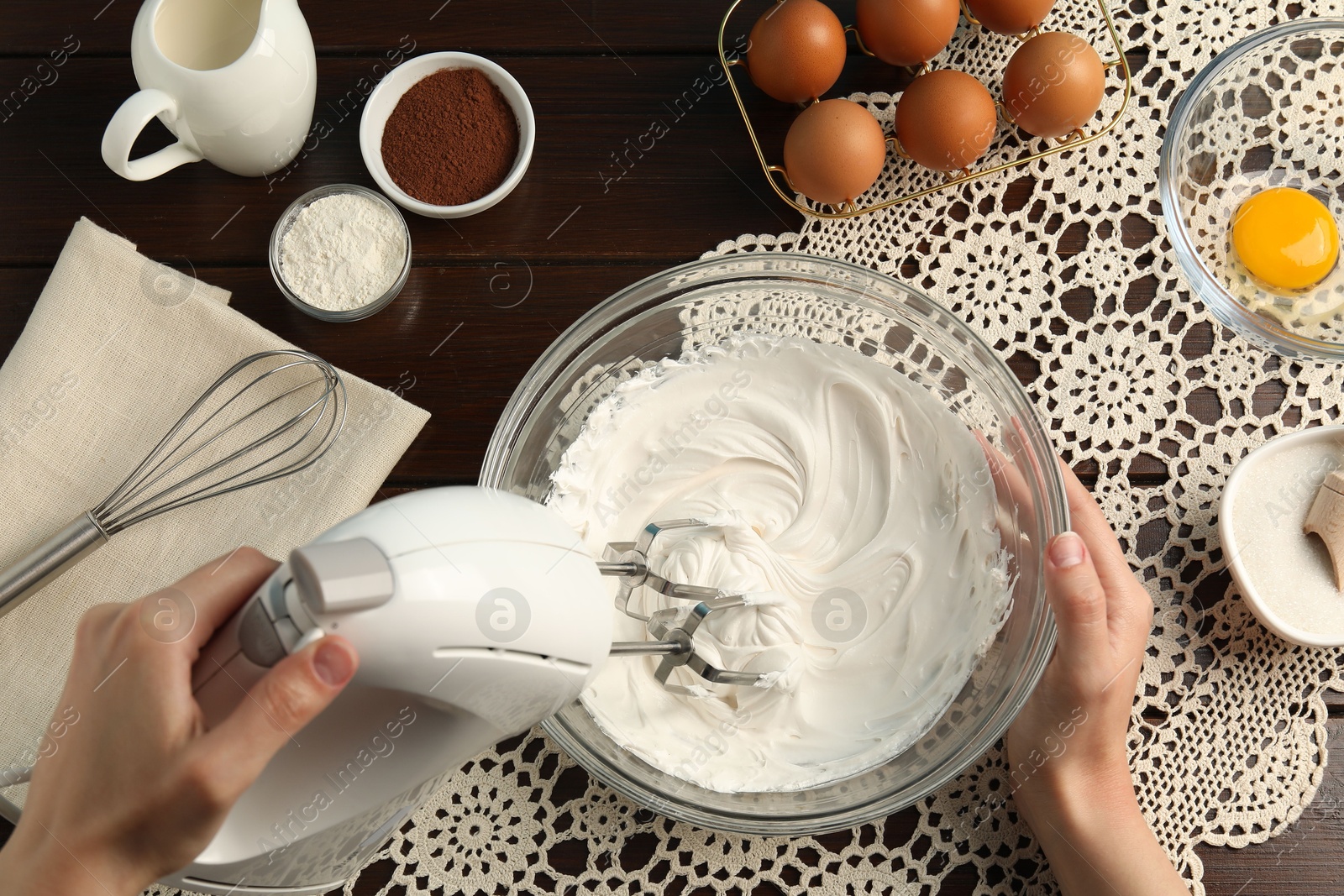 Woman whisking cream with hand mixer at wooden table, top view Photo of Woman whisking cream with hand mixer at wooden table, top view