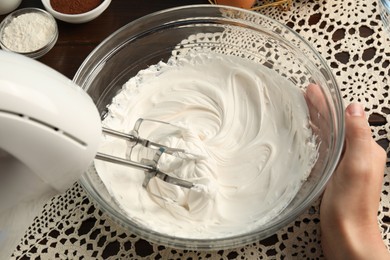 Photo of Woman whisking cream with hand mixer at table, closeup
