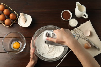 Photo of Woman whisking cream with hand mixer at wooden table, top view