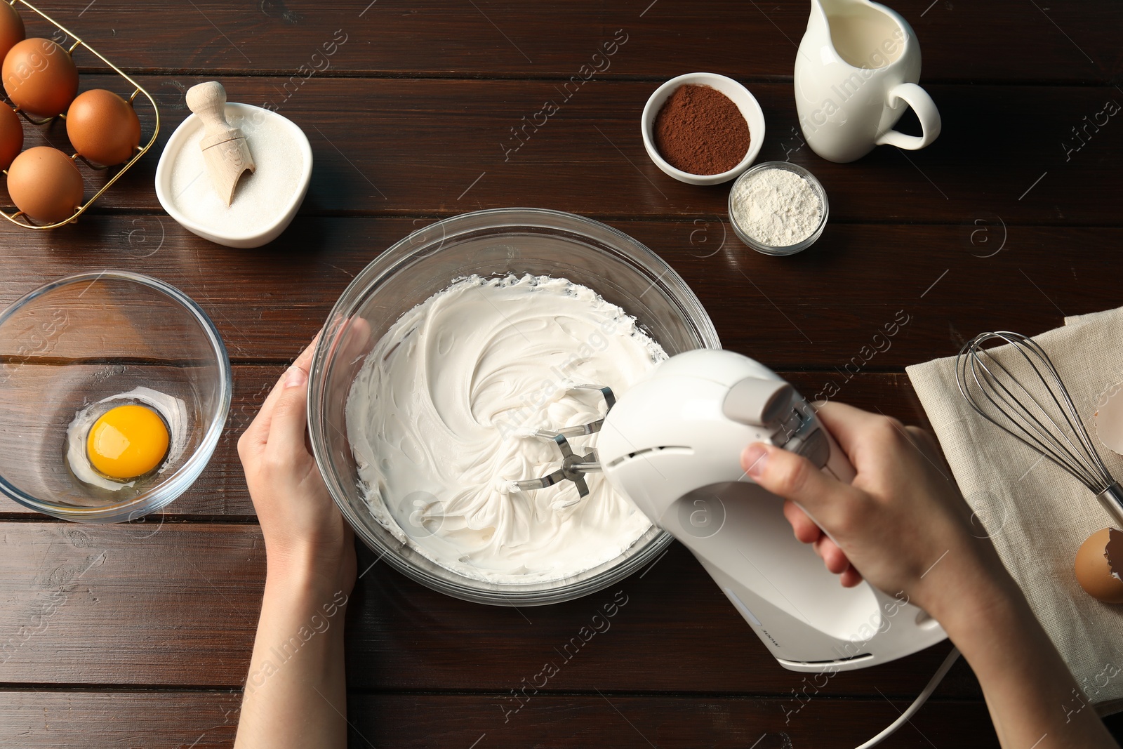 Woman whisking cream with hand mixer at wooden table, top view Photo of Woman whisking cream with hand mixer at wooden table, top view