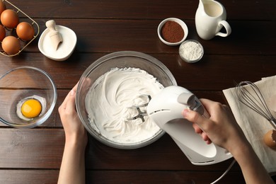 Photo of Woman whisking cream with hand mixer at wooden table, top view