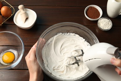 Photo of Woman whisking cream with hand mixer at wooden table, top view