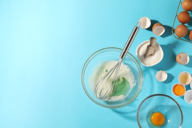 Photo of Egg whites in bowl, whisk, sugar and eggs on light blue table, flat lay. Space for text