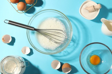 Photo of Whisk, egg whites in bowl and other products on light blue table, flat lay
