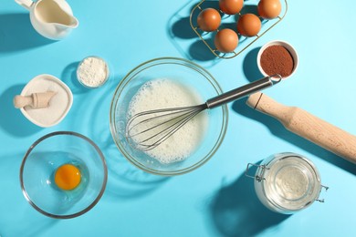 Photo of Whisk, egg whites in bowl and other products on light blue table, flat lay
