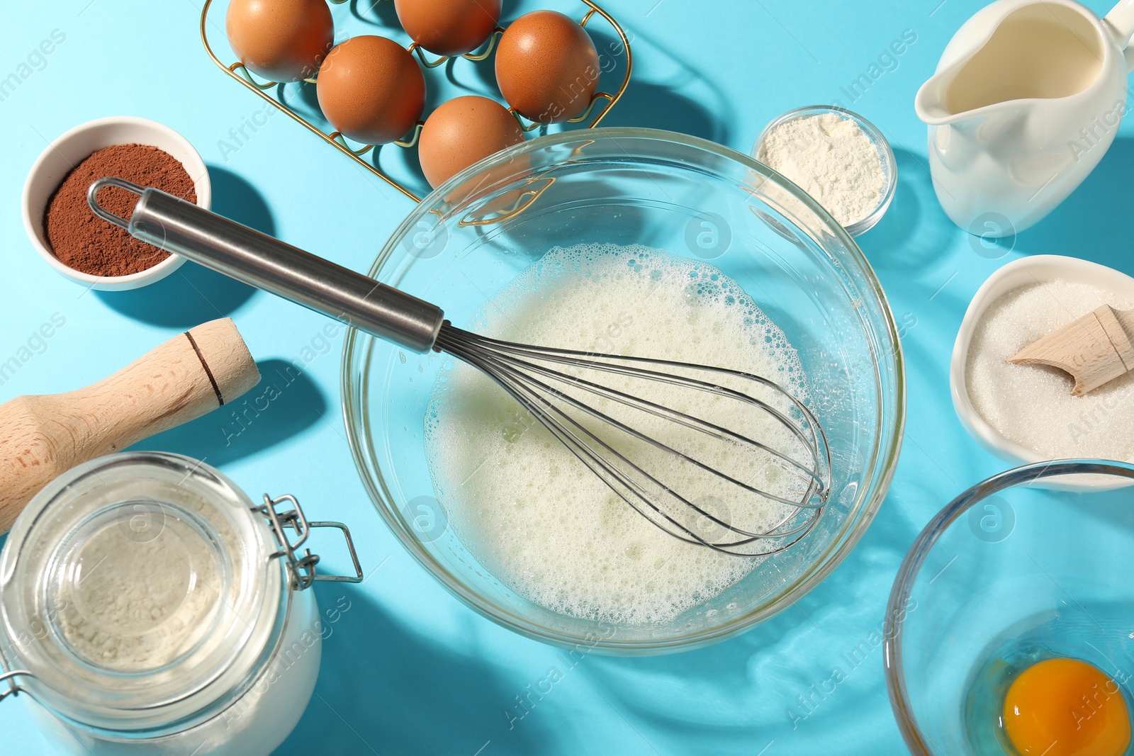 Whisk, egg whites in bowl and other products on light blue table, flat lay Photo of Whisk, egg whites in bowl and other products on light blue table, flat lay