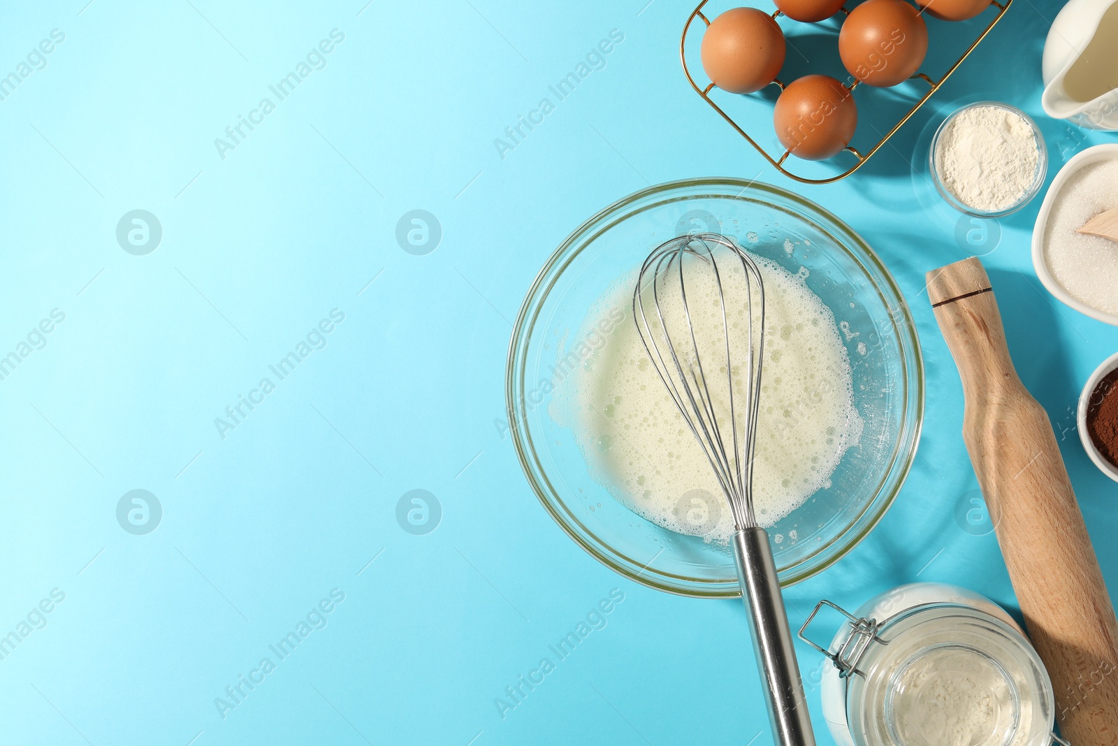 Whisk, egg whites in bowl and other products on light blue table, flat lay. Space for text Photo of Whisk, egg whites in bowl and other products on light blue table, flat lay. Space for text