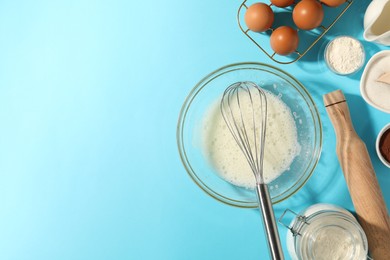 Photo of Whisk, egg whites in bowl and other products on light blue table, flat lay. Space for text