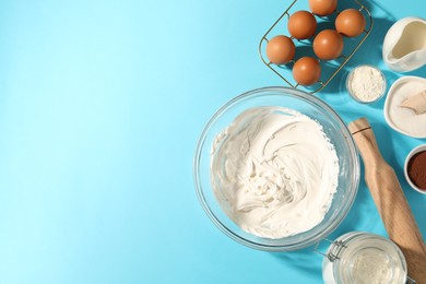 Photo of Whipped cream in bowl and other products on light blue table, flat lay. Space for text