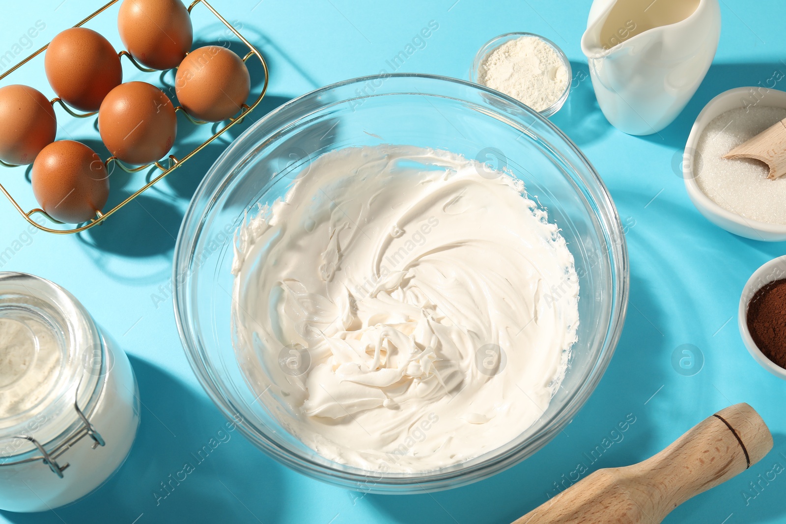 Whipped cream in bowl and other products on light blue table, above view Photo of Whipped cream in bowl and other products on light blue table, above view