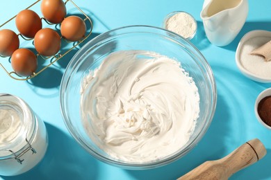 Photo of Whipped cream in bowl and other products on light blue table, above view
