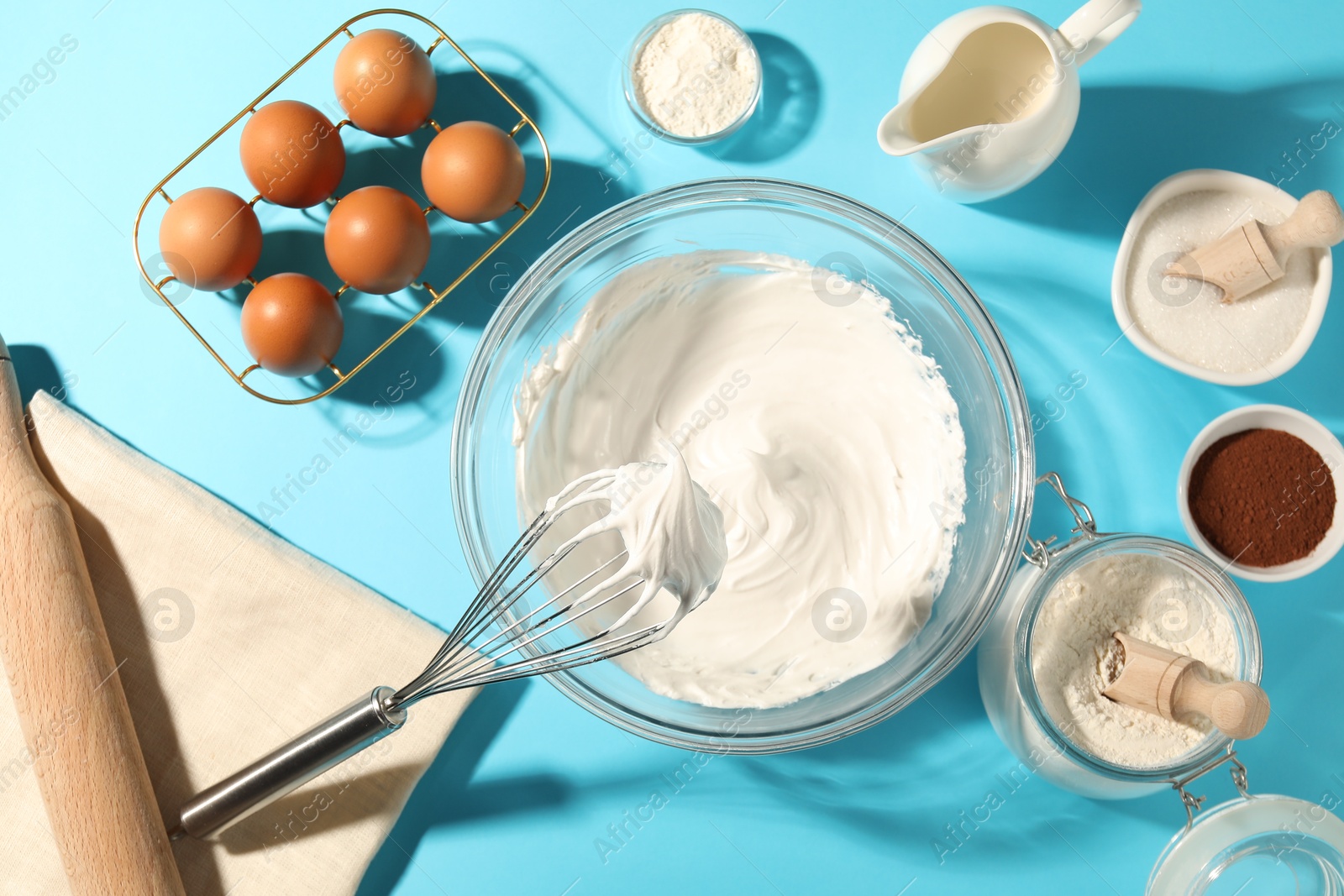 Whisk with whipped cream, eggs and other products on light blue table, flat lay Photo of Whisk with whipped cream, eggs and other products on light blue table, flat lay