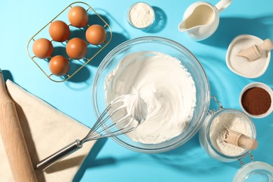 Photo of Whisk with whipped cream, eggs and other products on light blue table, flat lay