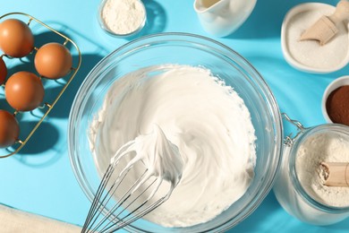 Photo of Whisk with whipped cream, eggs and other products on light blue table, flat lay