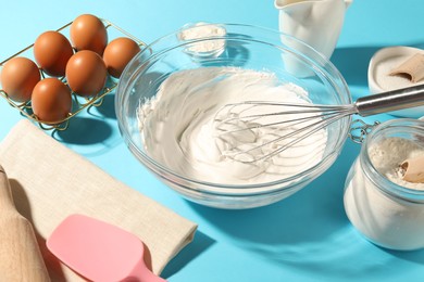 Photo of Whisk with whipped cream, eggs and other products on light blue table