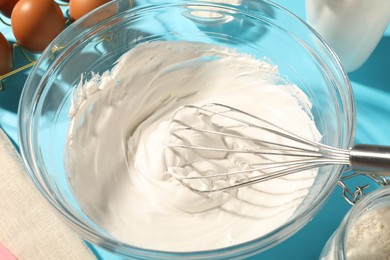 Photo of Whisk and whipped cream in bowl on light blue table, closeup