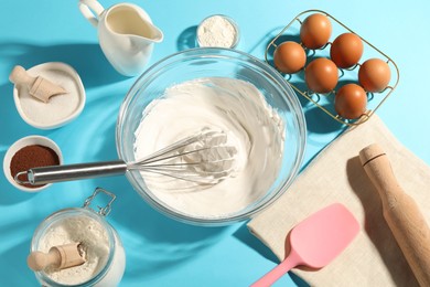 Photo of Whisk with whipped cream, eggs and other products on light blue table, flat lay