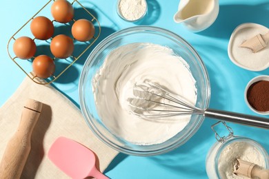 Photo of Whisk with whipped cream, eggs and other products on light blue table, flat lay
