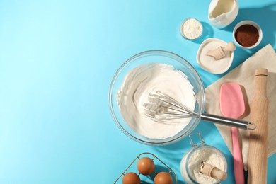 Photo of Whisk with whipped cream, eggs and other products on light blue table, flat lay. Space for text