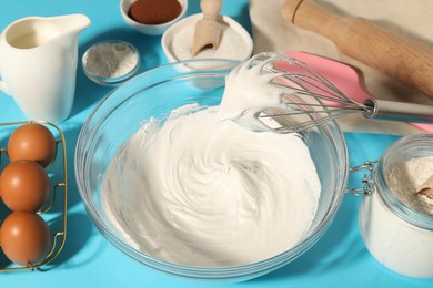 Photo of Whisk with whipped cream, eggs and other products on light blue table, closeup