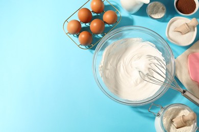 Photo of Whisk with whipped cream, eggs and other products on light blue table, flat lay. Space for text