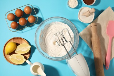 Photo of Hand mixer with whipped cream, eggs and other products on light blue table, flat lay