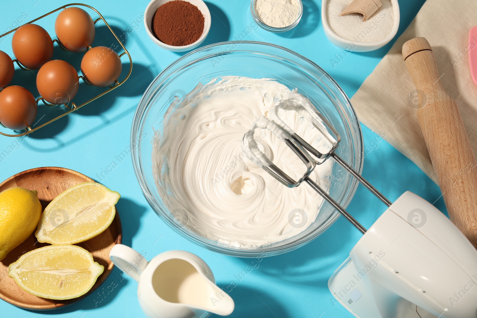 Hand mixer with whipped cream, eggs and other products on light blue table, flat lay Photo of Hand mixer with whipped cream, eggs and other products on light blue table, flat lay