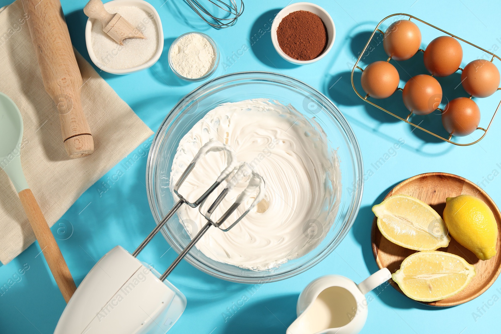 Hand mixer with whipped cream, eggs and other products on light blue table, flat lay Photo of Hand mixer with whipped cream, eggs and other products on light blue table, flat lay