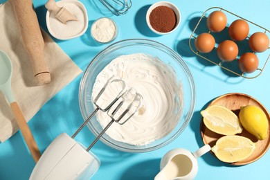 Photo of Hand mixer with whipped cream, eggs and other products on light blue table, flat lay