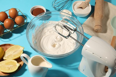 Photo of Hand mixer with whipped cream, eggs and other products on light blue table, closeup