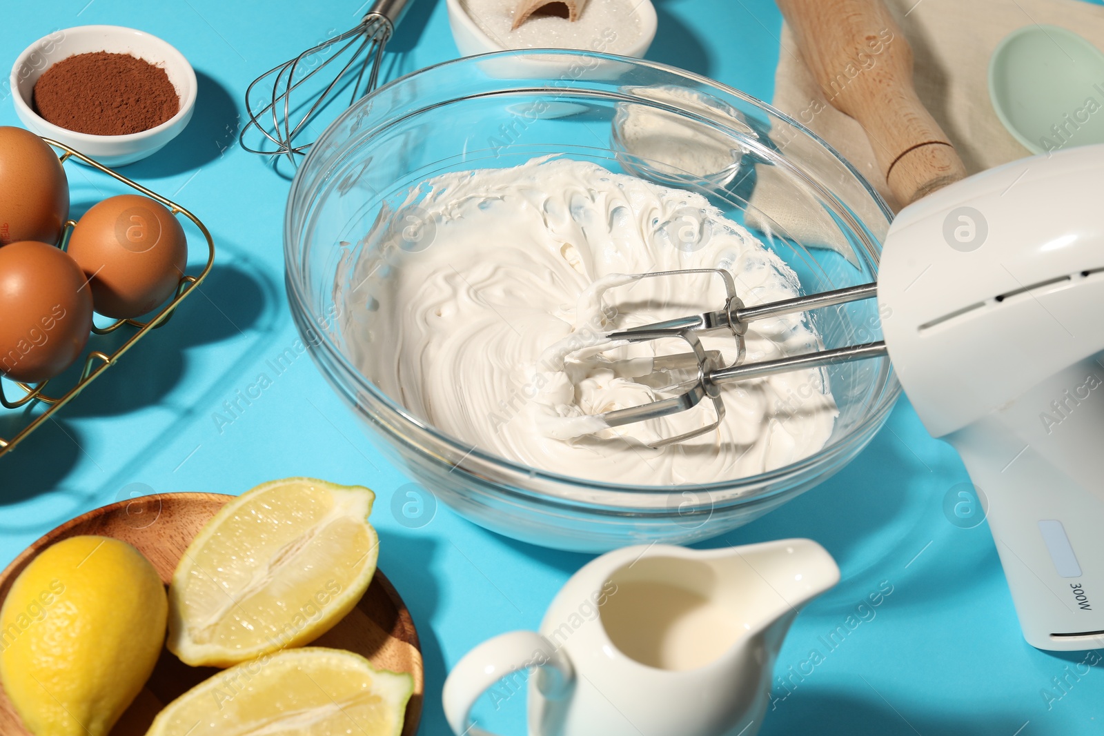 Hand mixer with whipped cream, eggs and other products on light blue table, closeup Photo of Hand mixer with whipped cream, eggs and other products on light blue table, closeup