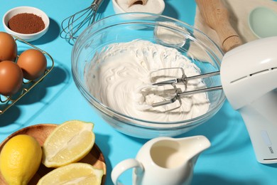 Photo of Hand mixer with whipped cream, eggs and other products on light blue table, closeup