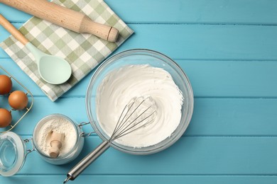 Photo of Whisk, whipped cream in bowl, eggs and flour on light blue wooden table, flat lay