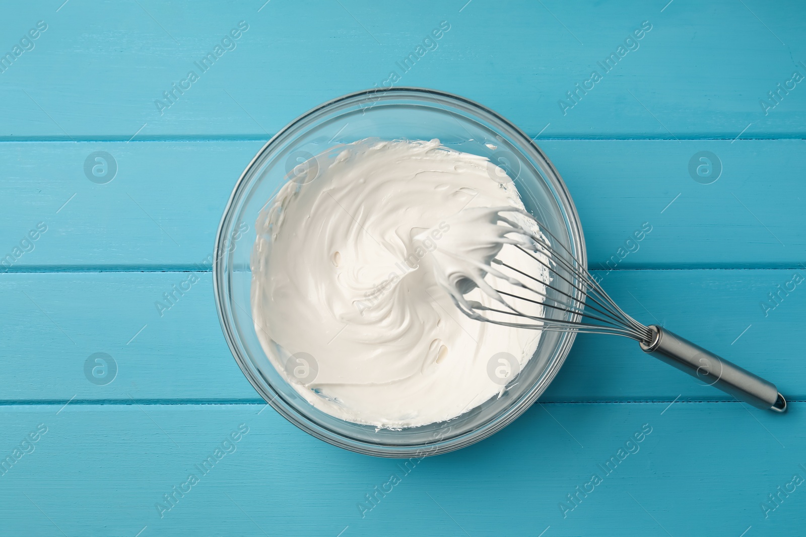 Whisk and whipped cream in bowl on light blue wooden table, top view Photo of Whisk and whipped cream in bowl on light blue wooden table, top view