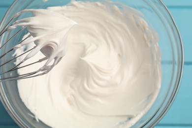 Photo of Whisk with whipped cream above bowl on table, top view